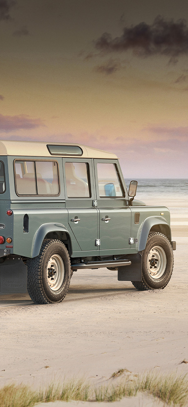 A green Defender V8 on the beach.